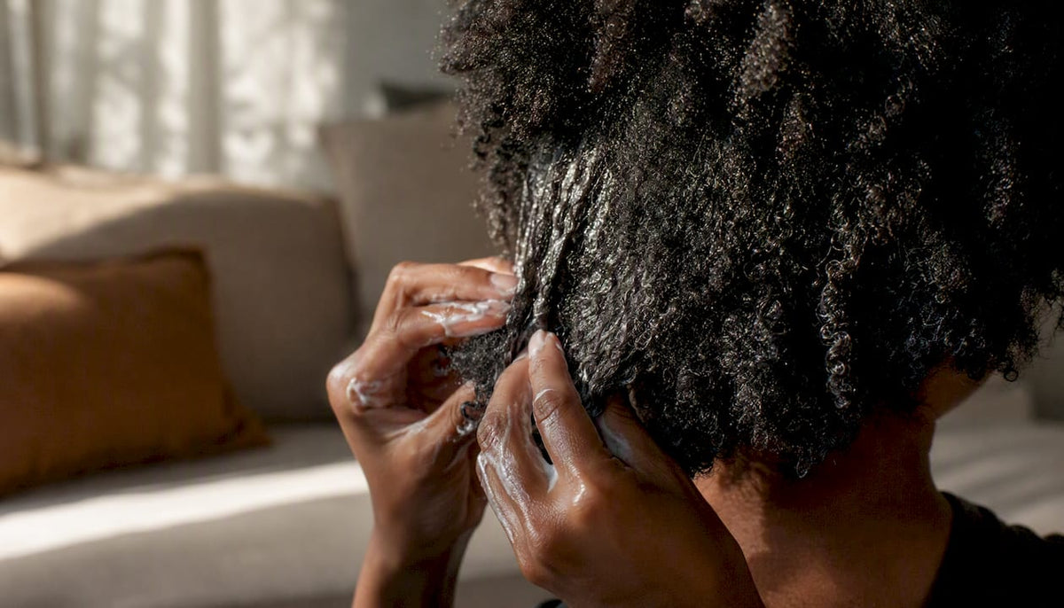 Hands applying creamy hair product to curly hair