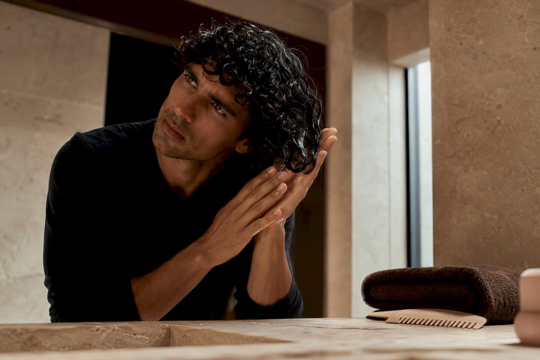 Man styling damp curls in bathroom