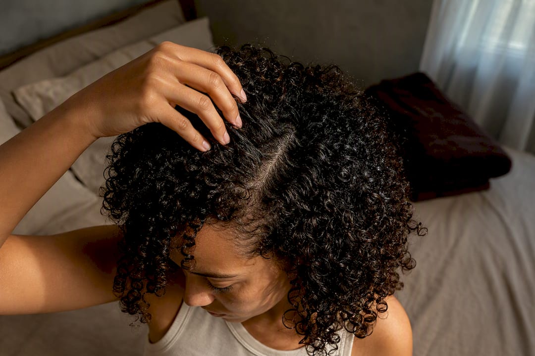 Woman inspecting scalp beneath curly hair