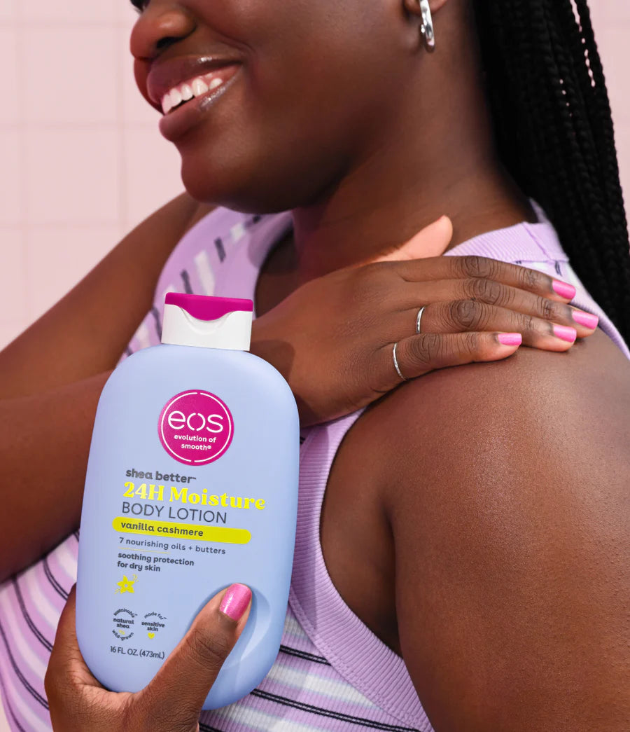 Woman holding an eos body lotion bottle against a pink background