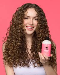 Woman with curly hair holding a bottle of 'Bumble and Bumble' product against a pink background